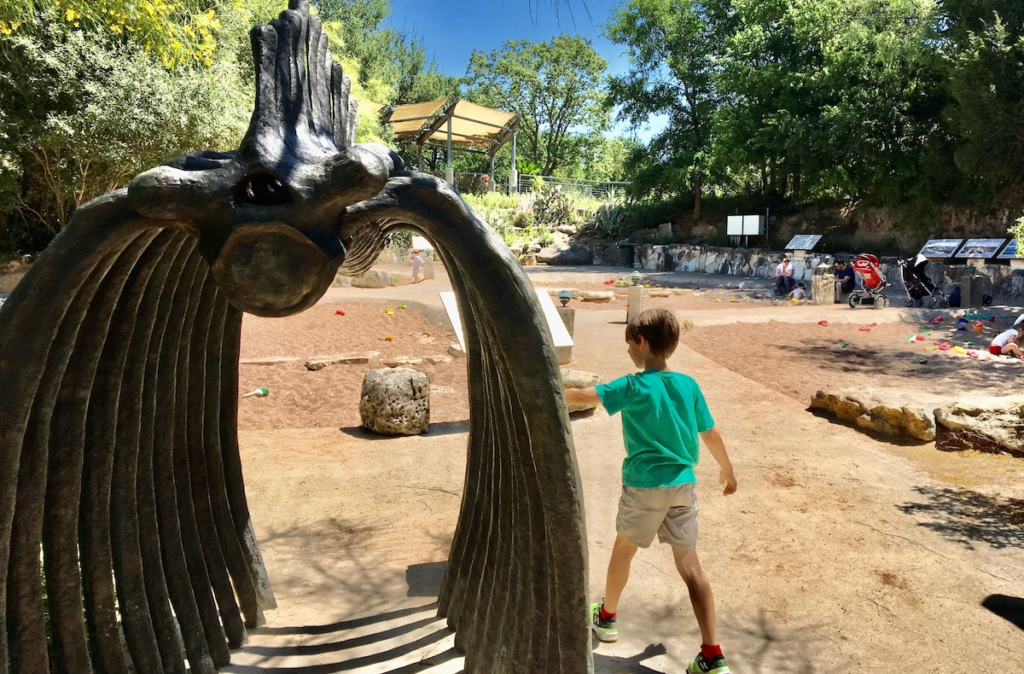 Kid standing next to a dinosaur skeleton